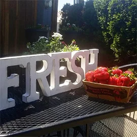 A three dinemsional sign that sys FRESH sits behind a bowl of fresh Strawberries