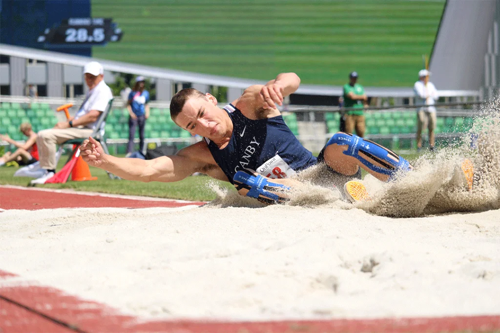 A student lands in the sand after a long jump