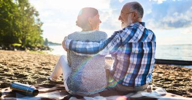 An eldeerly cpouple sit on the beach at sunset