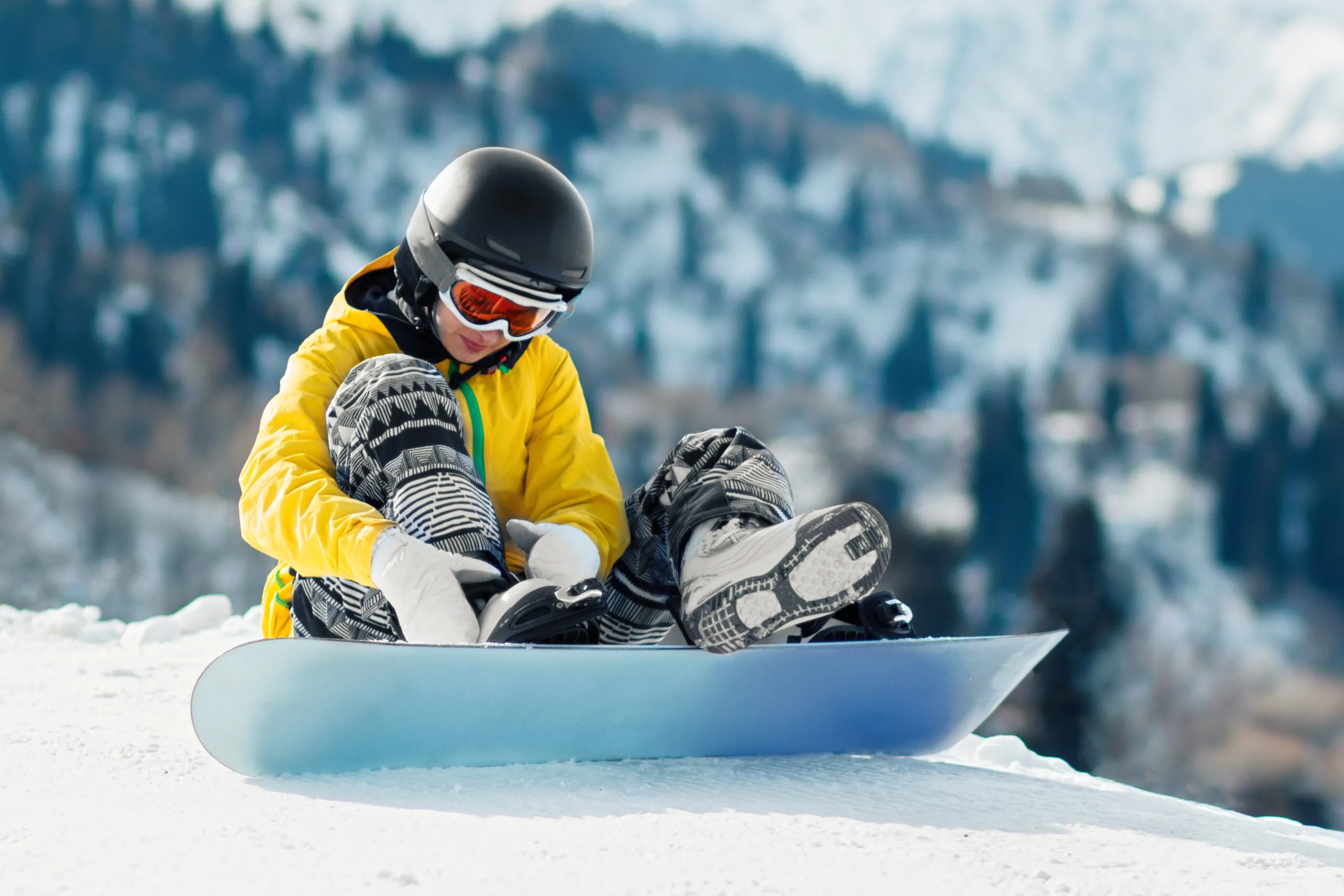 A woman adjusts her snowboard boots